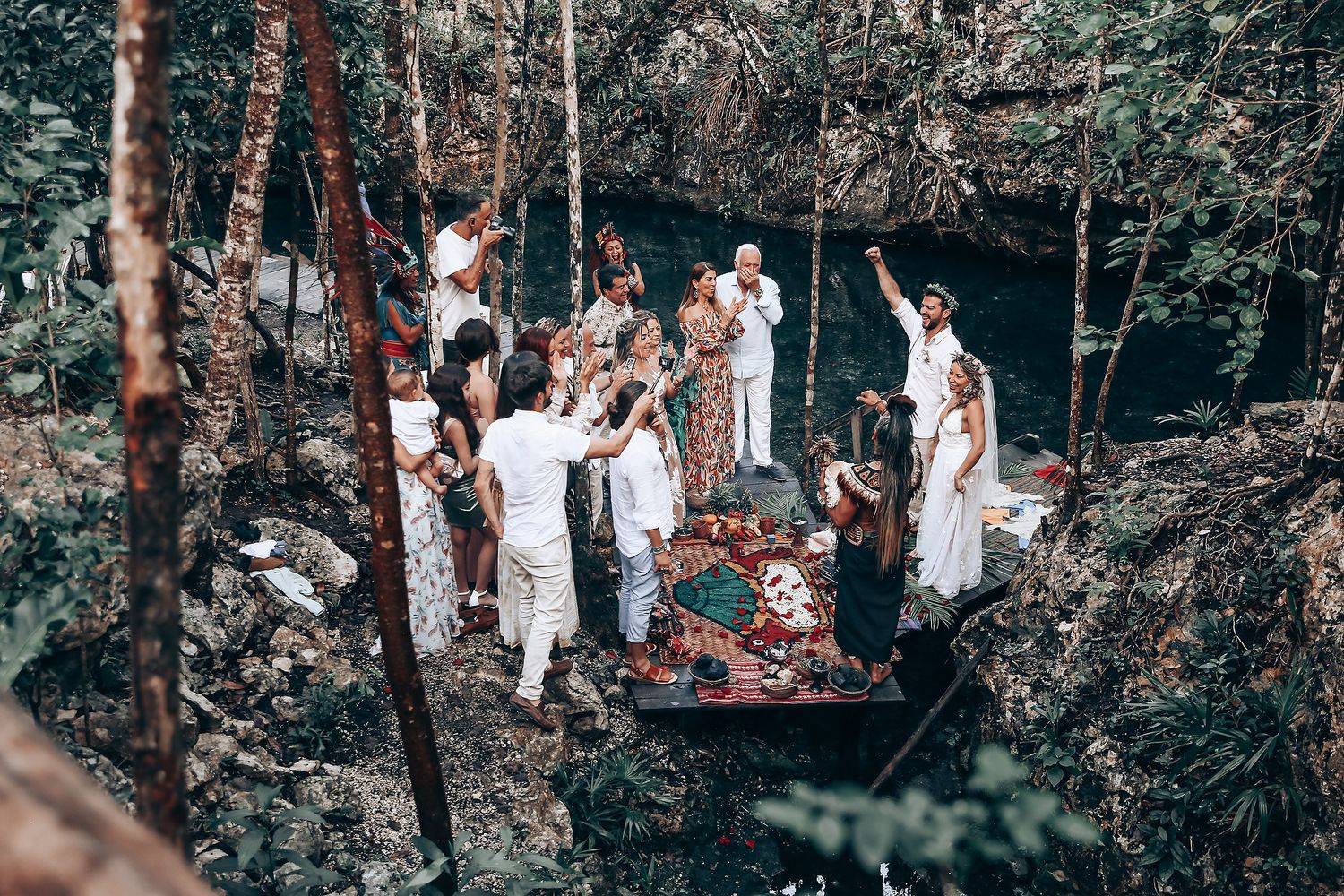 Wedding attendees in white outfits gather among trees during an outdoor forest celebration.