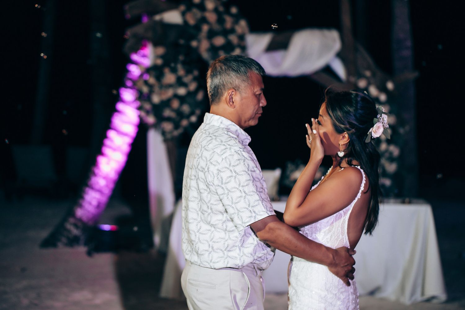 An emotional moment captured during a wedding reception with purple lighting.