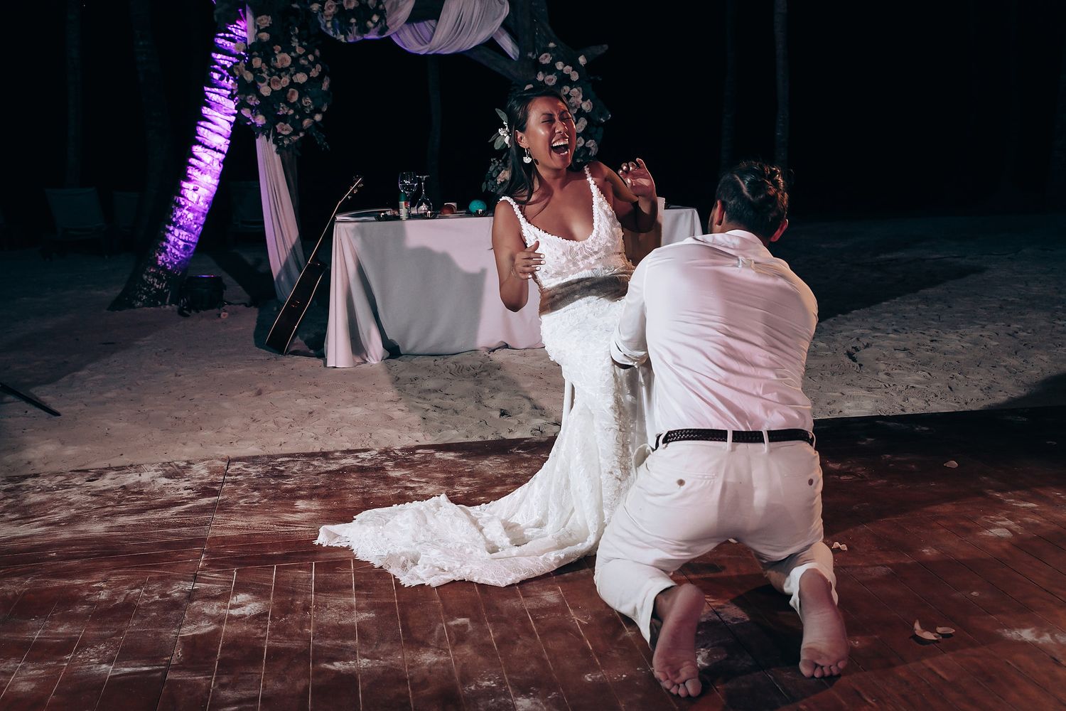 A touching wedding proposal moment on a wooden dance floor with purple lighting.