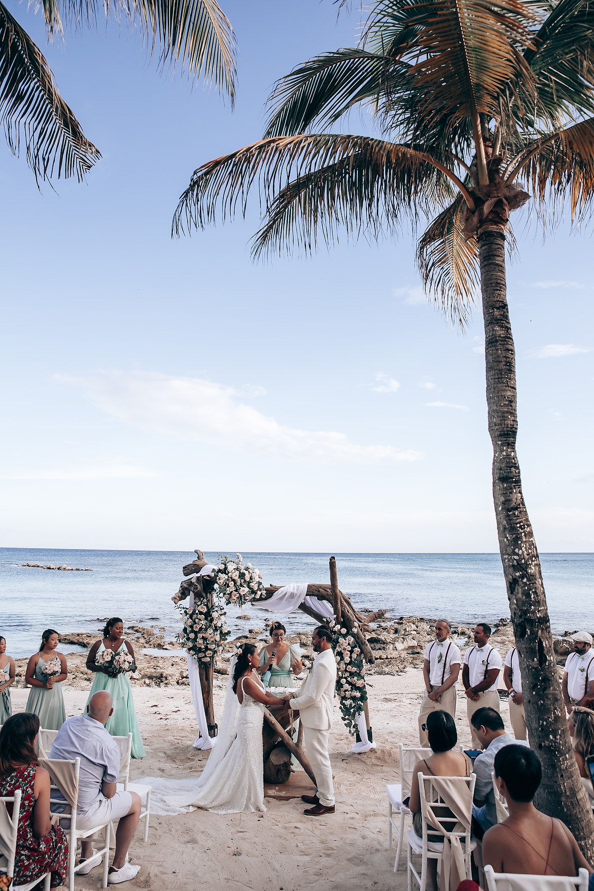 Beachside wedding ceremony with palm trees and ocean backdrop.