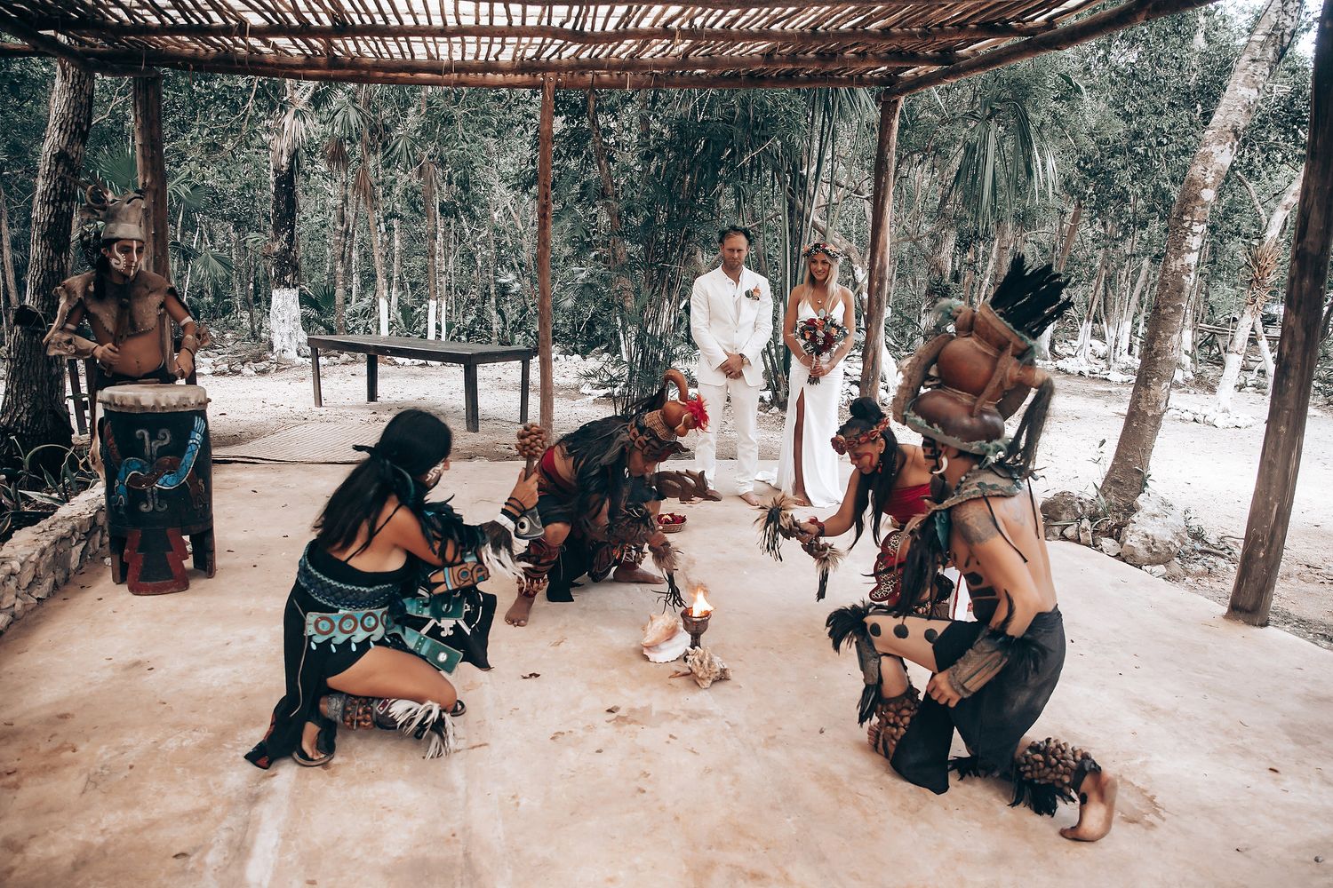 Traditional Mayan ceremony performers kneel during a spiritual ritual under a wooden pergola.