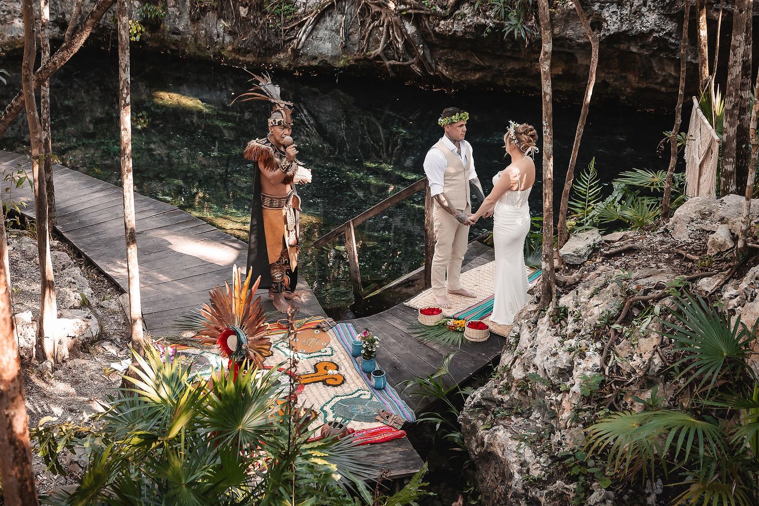 Couple exchanges vows at a lush jungle cenote wedding ceremony with a Mayan officiant in traditional attire.