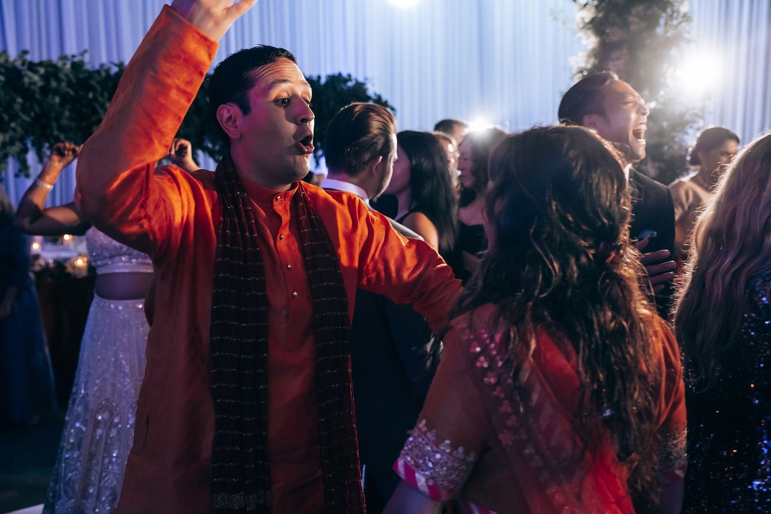 Wedding reception dance party with colorful lighting and guests celebrating.