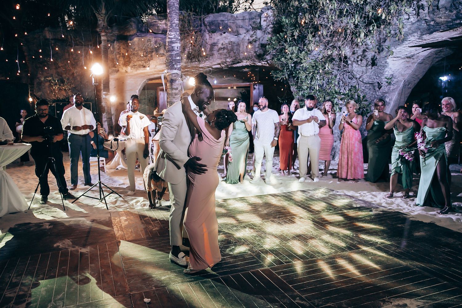 Evening beach wedding reception with illuminated dance floor and celebrating guests.