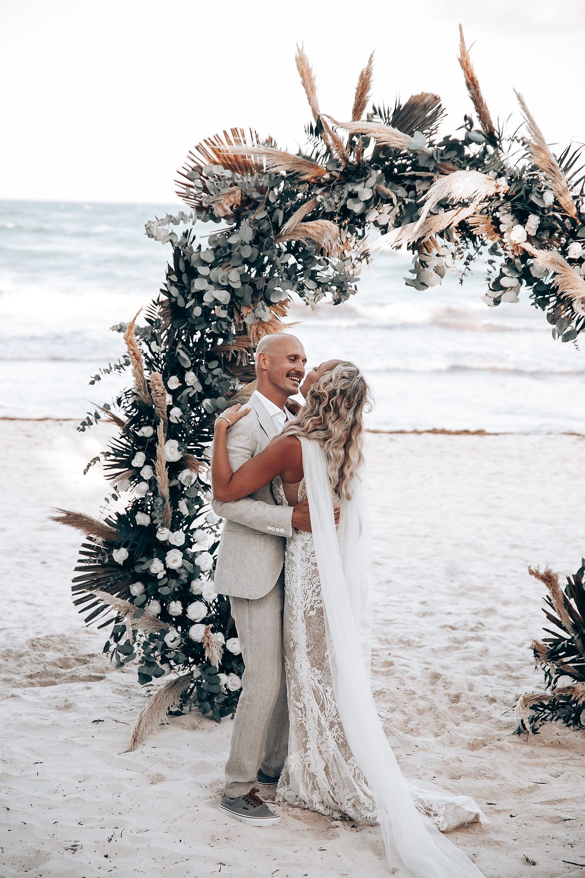 A beach wedding ceremony under an elegant floral arch with ocean waves in the background.
