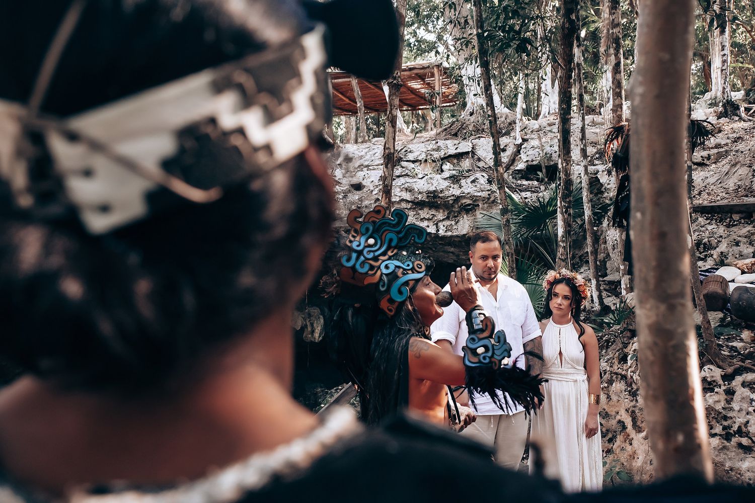 Wedding guests gather outdoors under tall trees during a forest ceremony celebration.