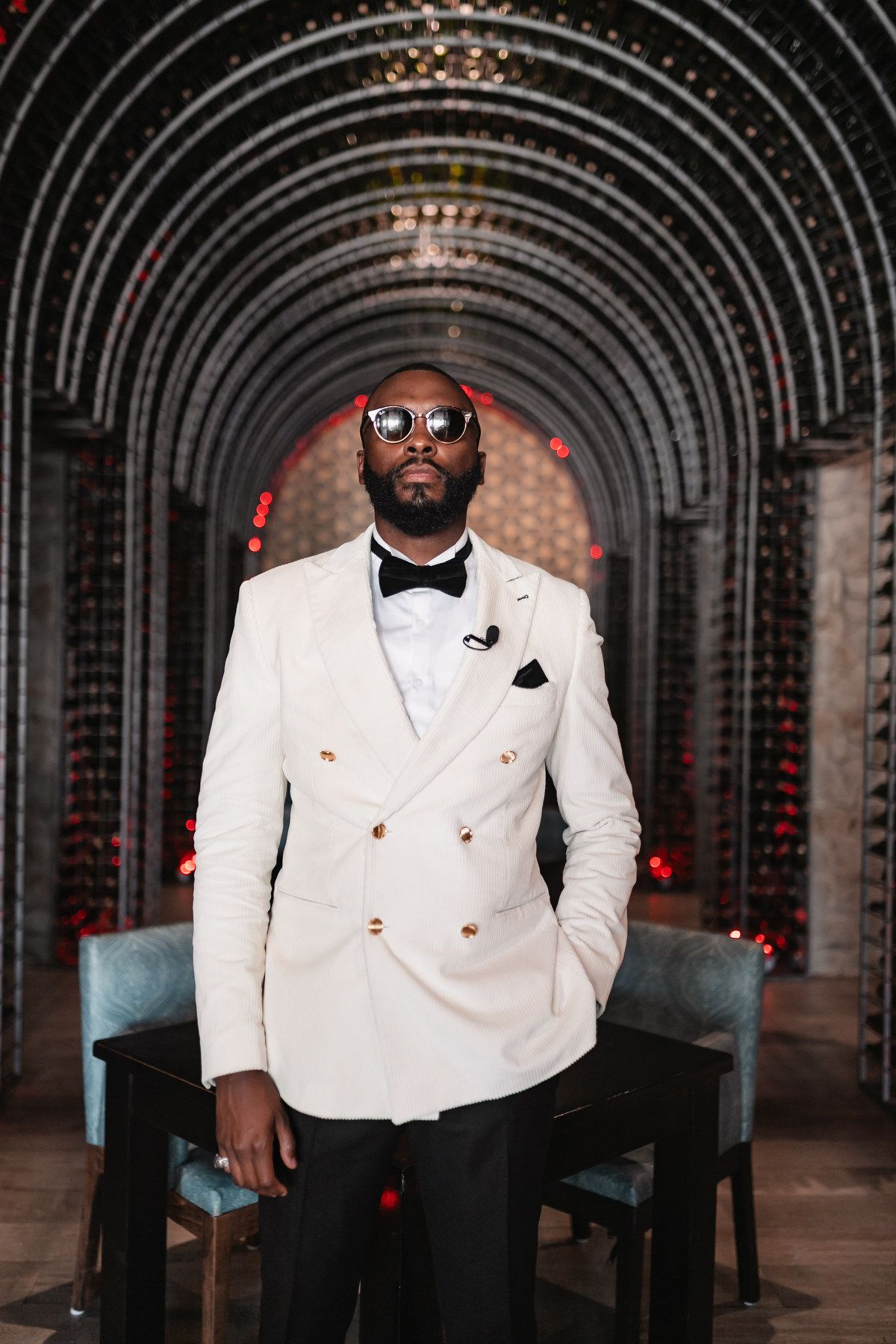Groom in a white double-breasted suit and bow tie posing in an elegant venue.