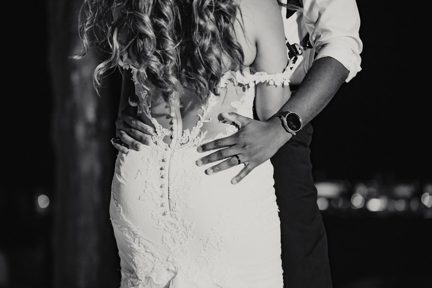 Black and white romantic close-up of couple embracing, bride in backless lace wedding dress.