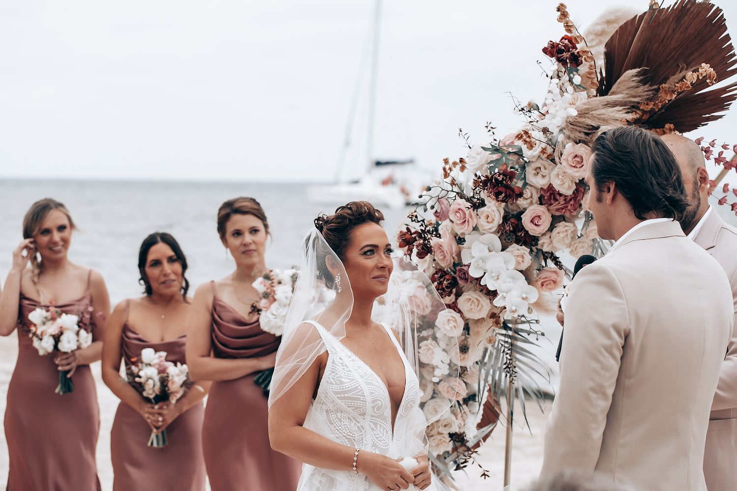 Wedding party gathered under a modern arch with dried floral arrangements by the ocean.