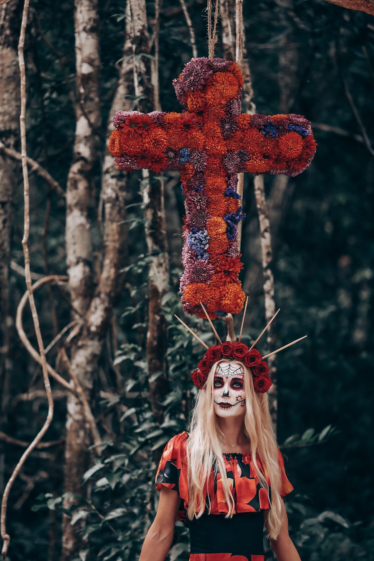 Large red floral cross decoration in dark forest setting for gothic themed event.
