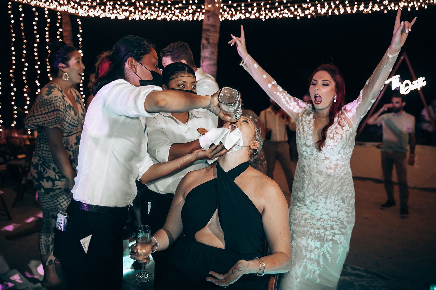 Wedding reception party with guests dancing under string lights at night.