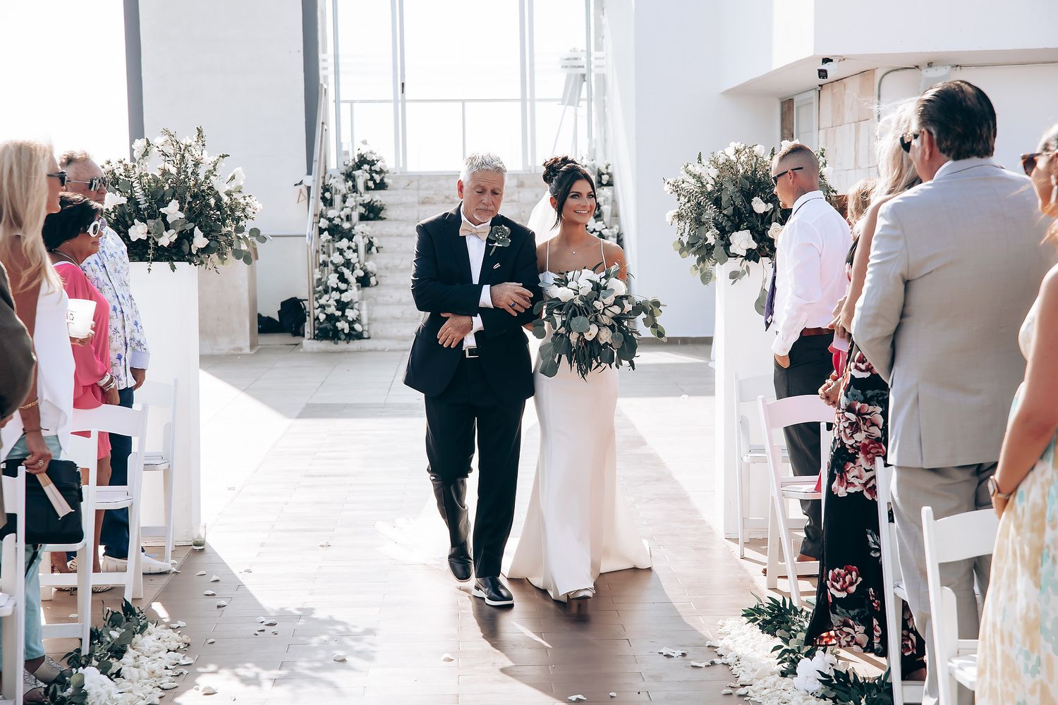 Elegant outdoor wedding ceremony setup with white chairs and floral decorations.
