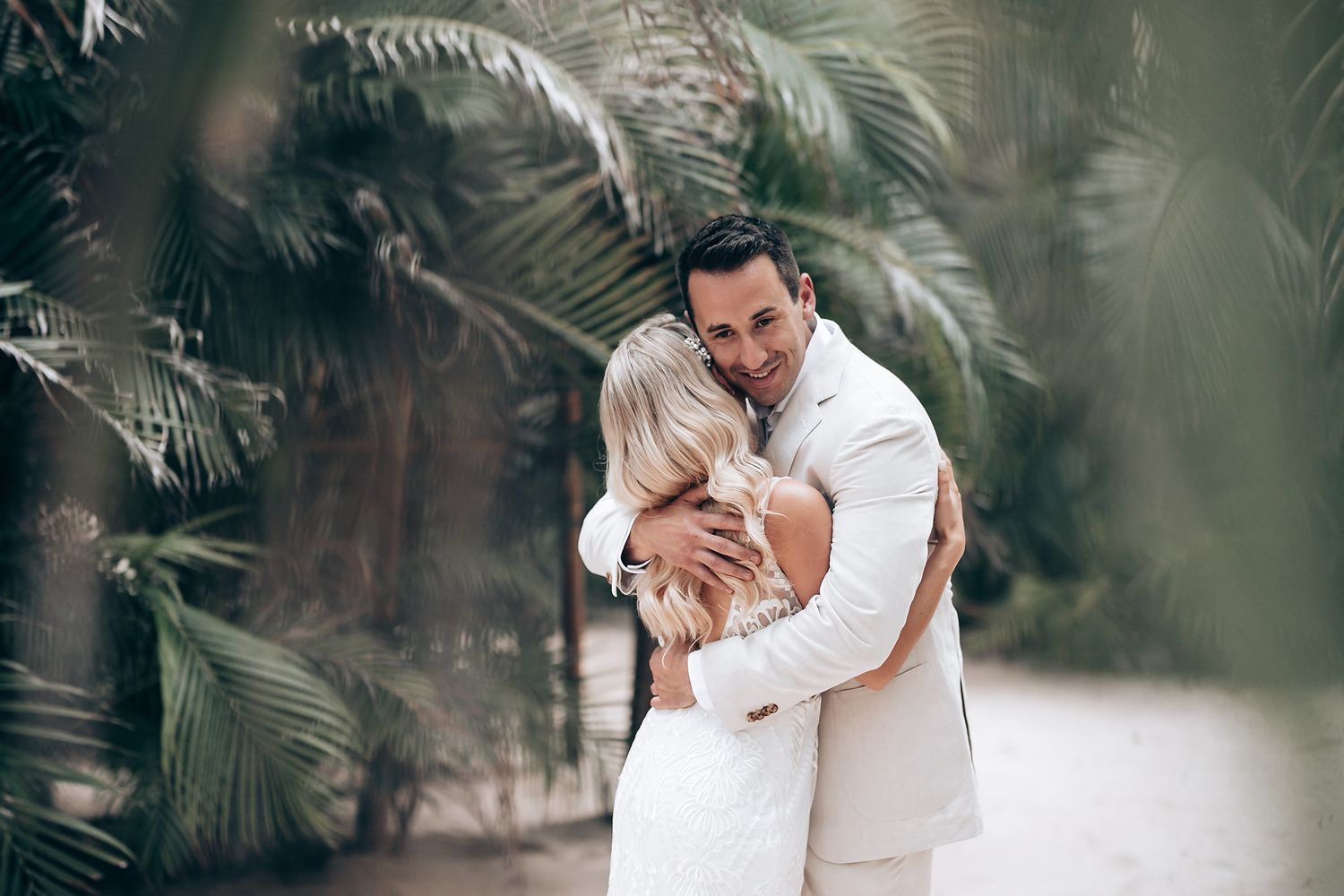 Romantic embrace under tropical palm trees during a destination wedding.