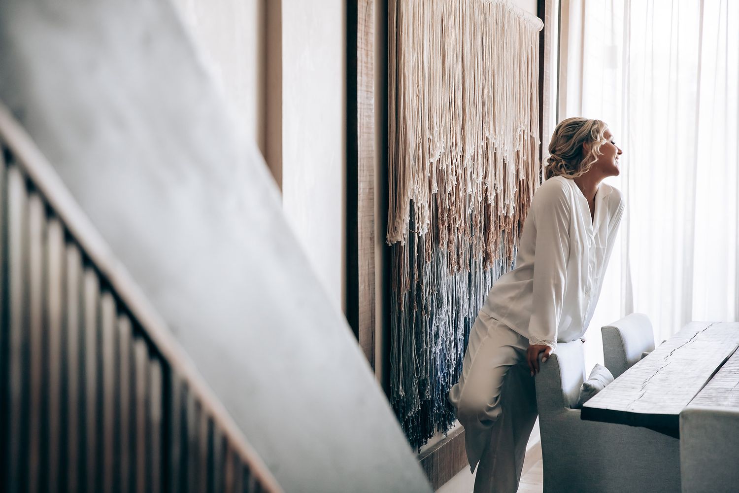 A white wedding gown with flowing fabric is displayed in front of a weathered wooden wall and railing.