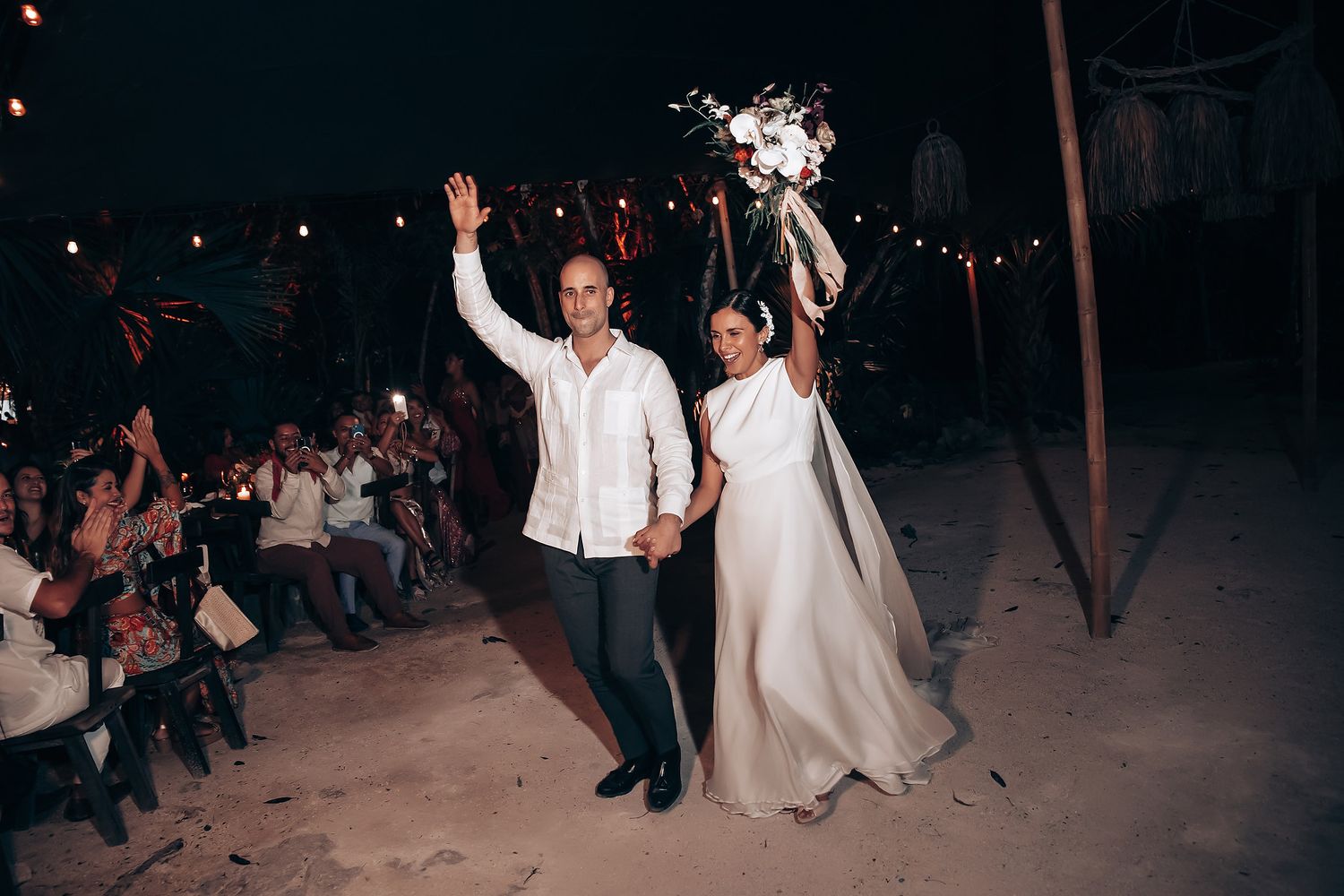 Silhouettes of wedding guests dance and celebrate on a dark dance floor illuminated by red lights.