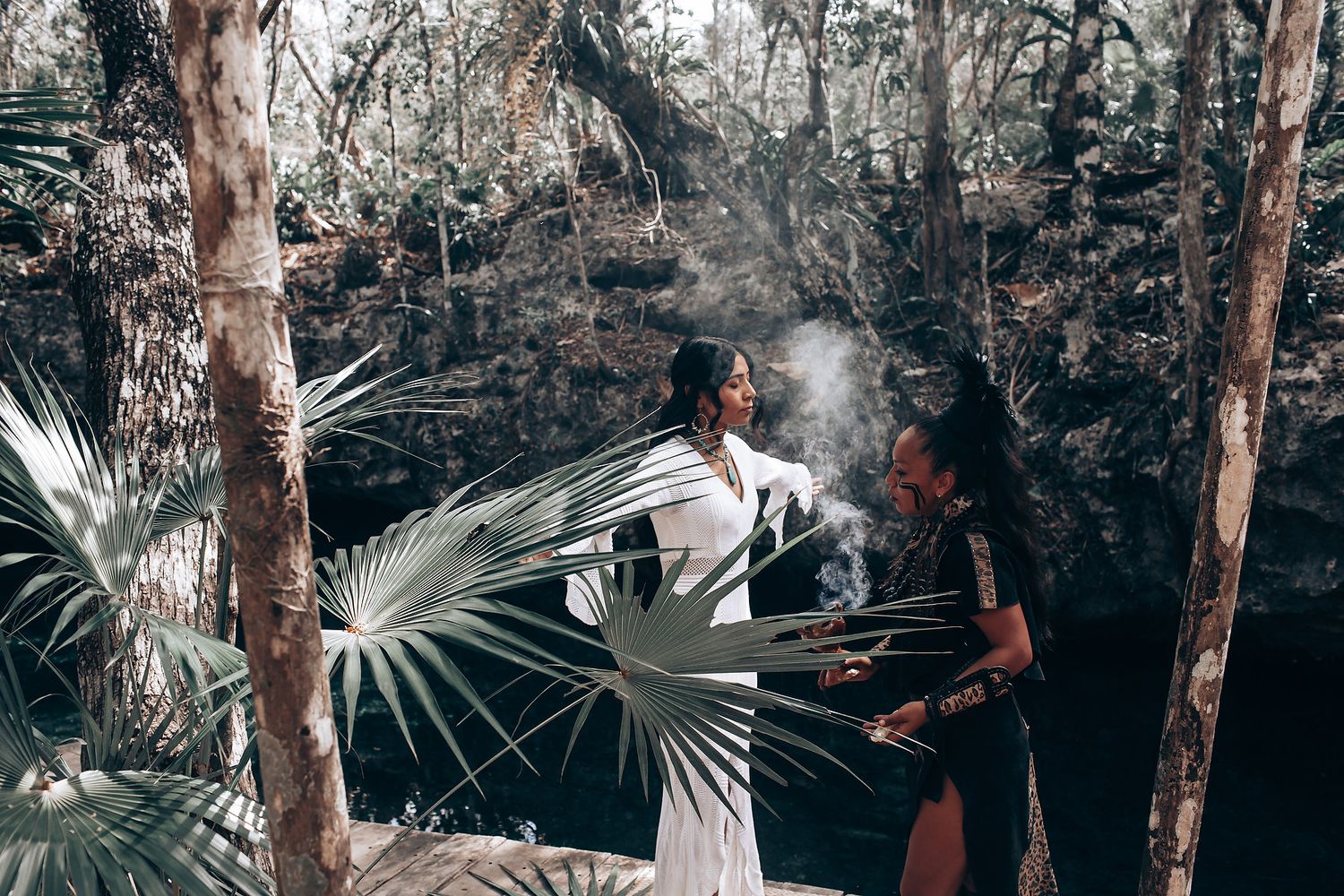 A couple shares a romantic moment in a tropical forest setting surrounded by palm trees and natural light.