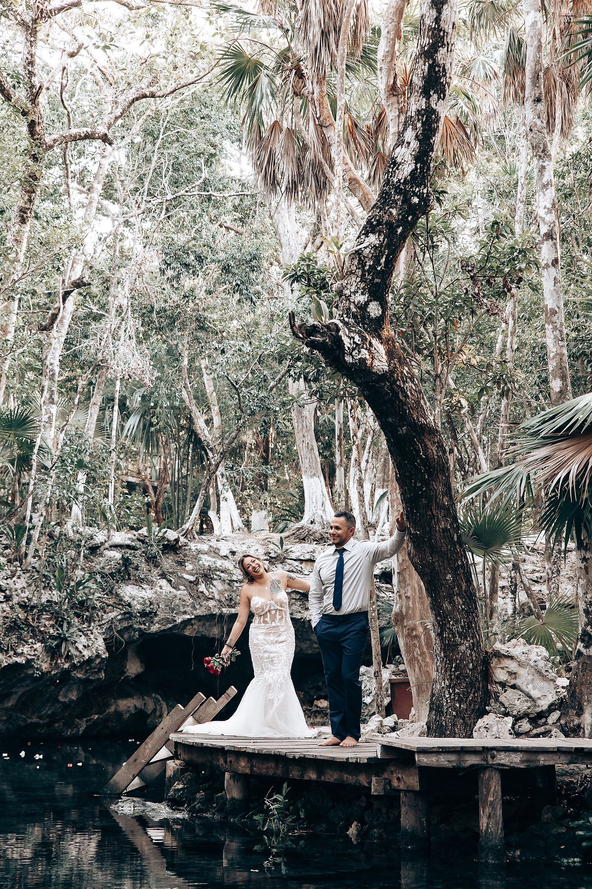 Artistic wedding photo shoot on a wooden platform over a natural cenote in a tropical forest.