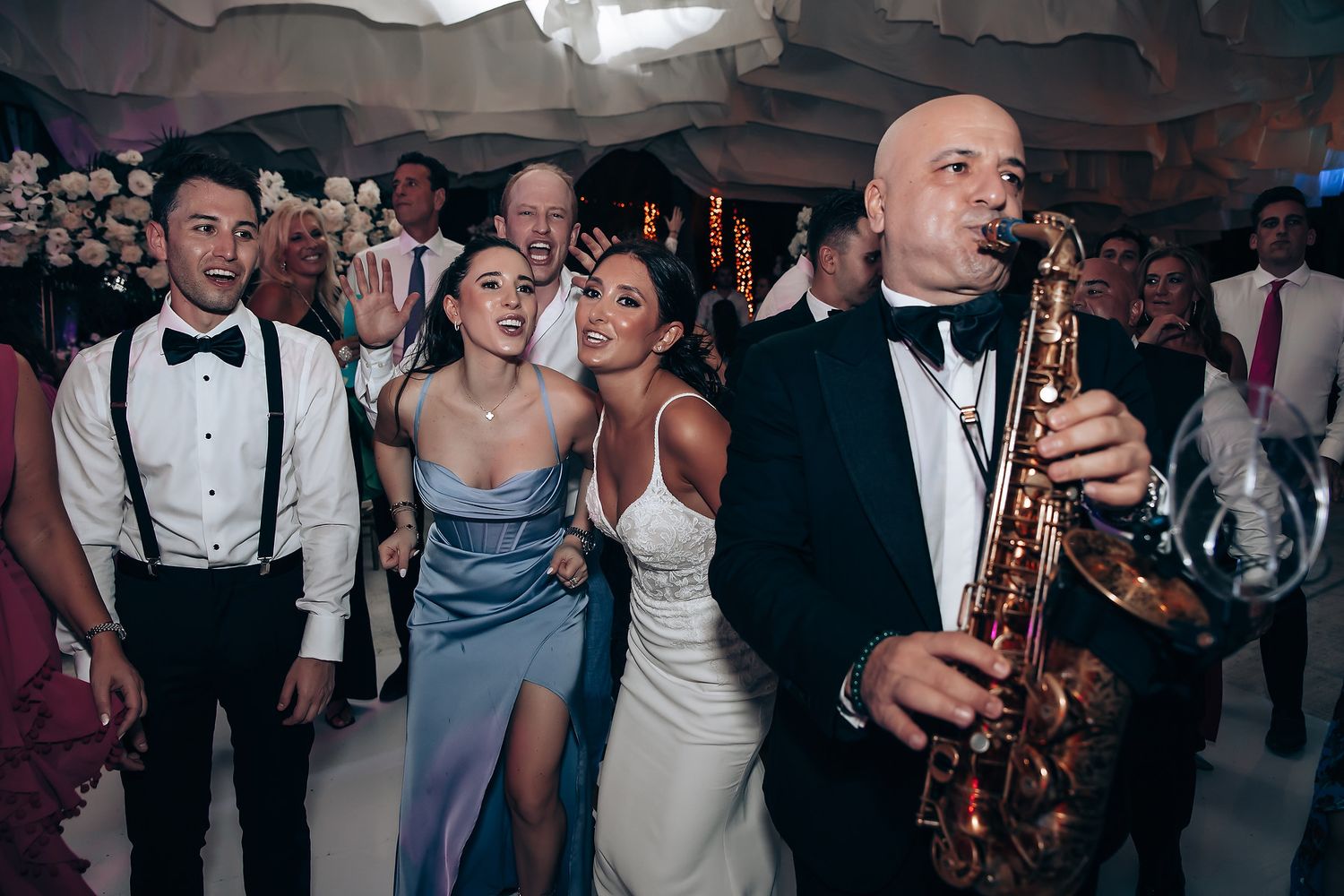 Wedding reception dance party with guests celebrating under decorative lighting.