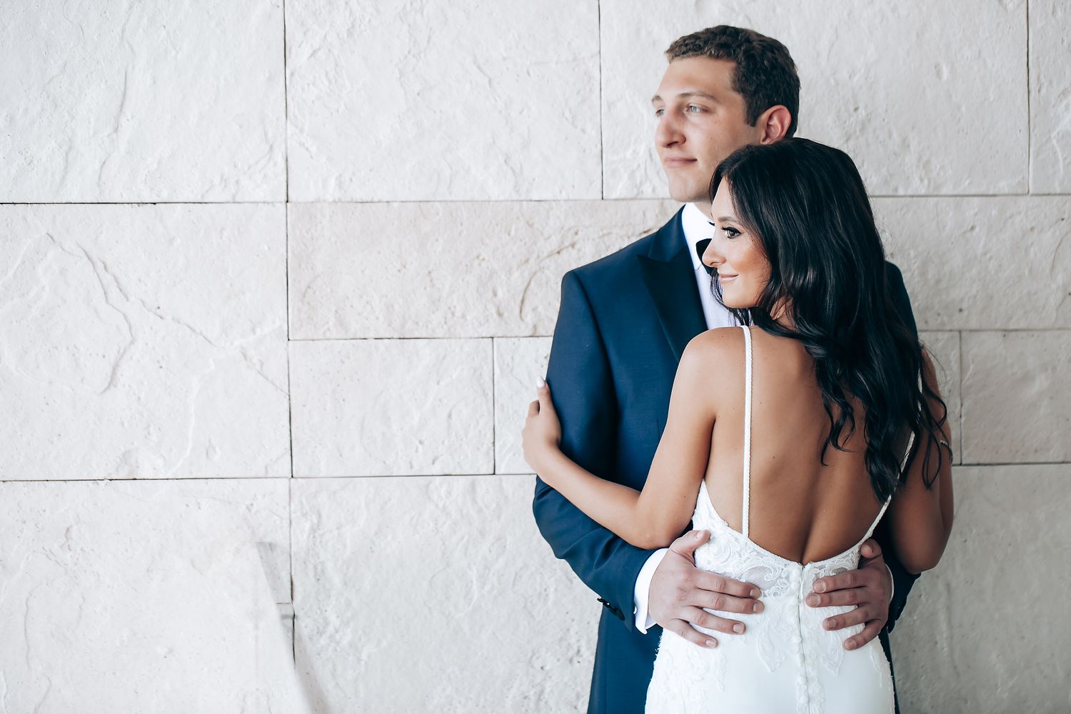 Romantic wedding portraits against white textured wall showing tender moments between newlyweds.