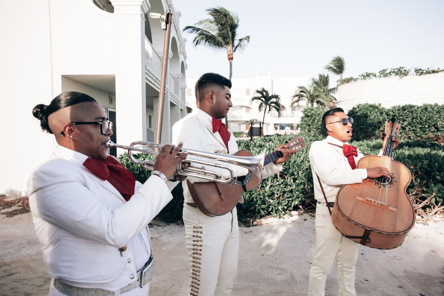 Mariachi band in traditional white and red uniforms playing trumpet and guitar outdoors.