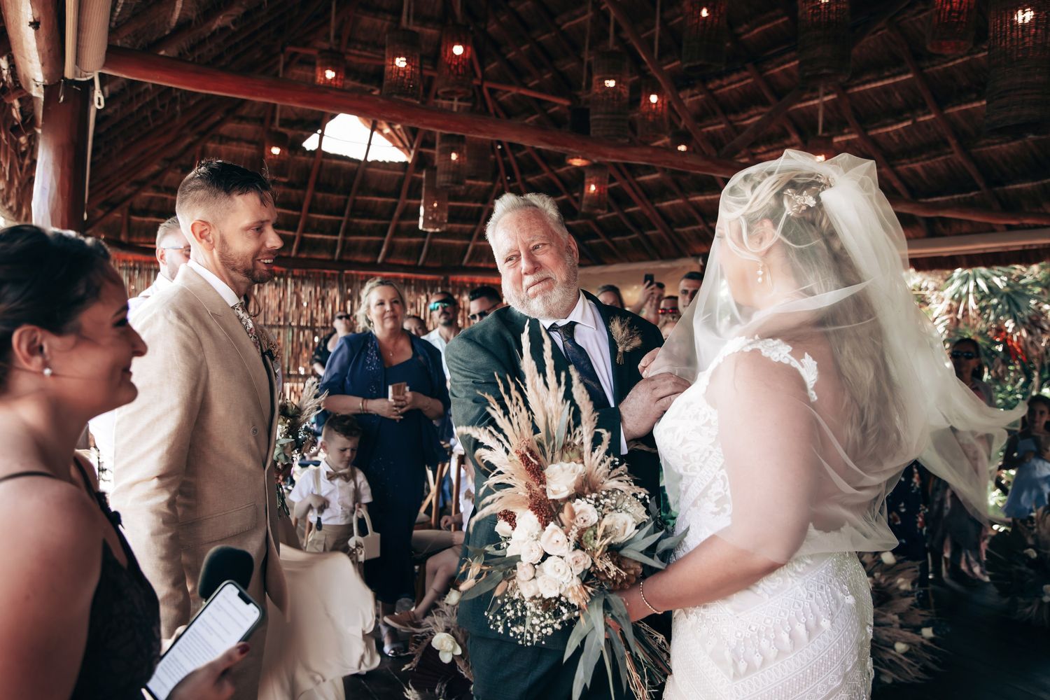 Bride and groom share a joyful moment during wedding ceremony in rustic barn venue with guests celebrating in background.