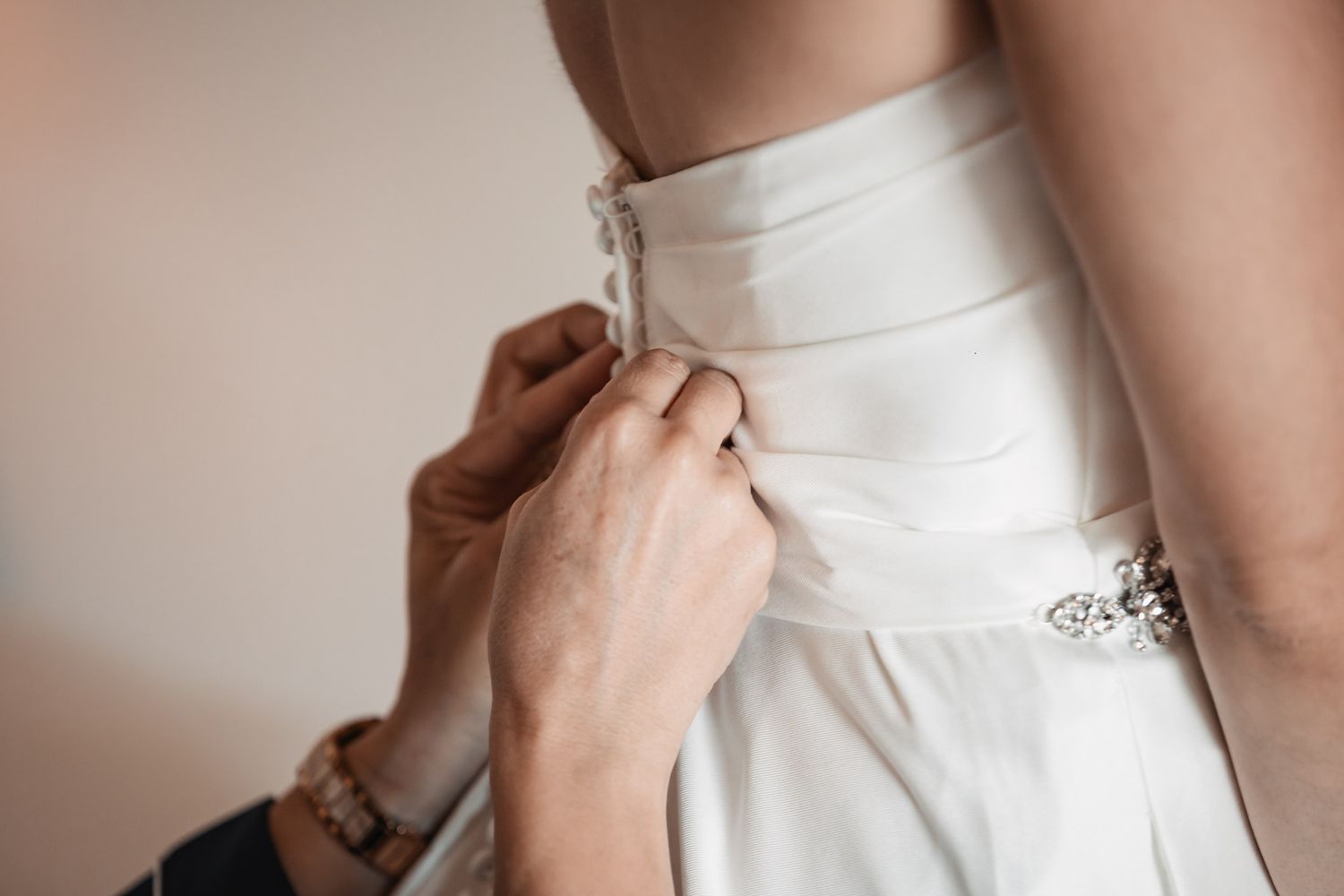 Close-up of hands fastening buttons on the back of a white wedding dress.