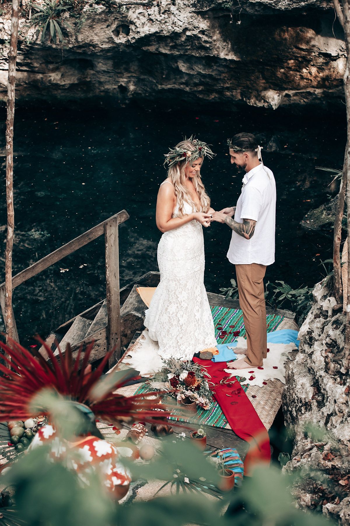 Intimate ceremony moment captured in a natural cave setting with red floral accents.