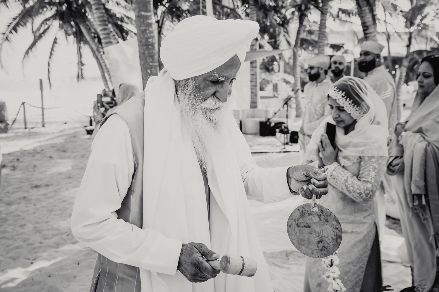 Black and white photo of elderly Sikh priest performing traditional Indian wedding rituals on beach.