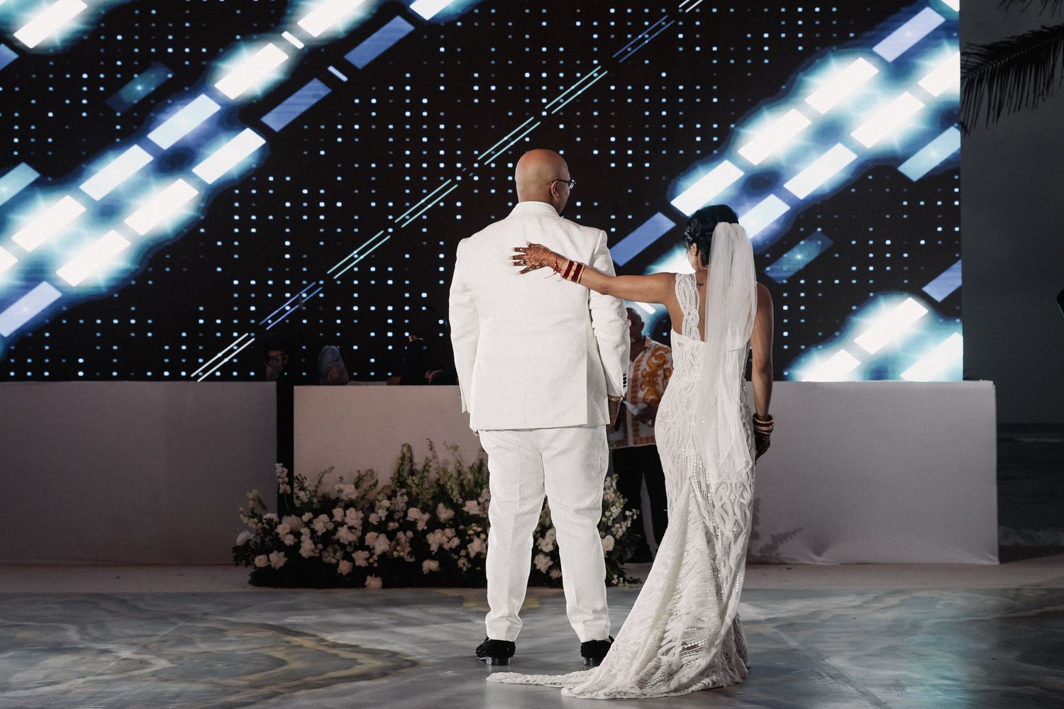Bride and groom share first dance before glittering backdrop at elegant wedding reception.