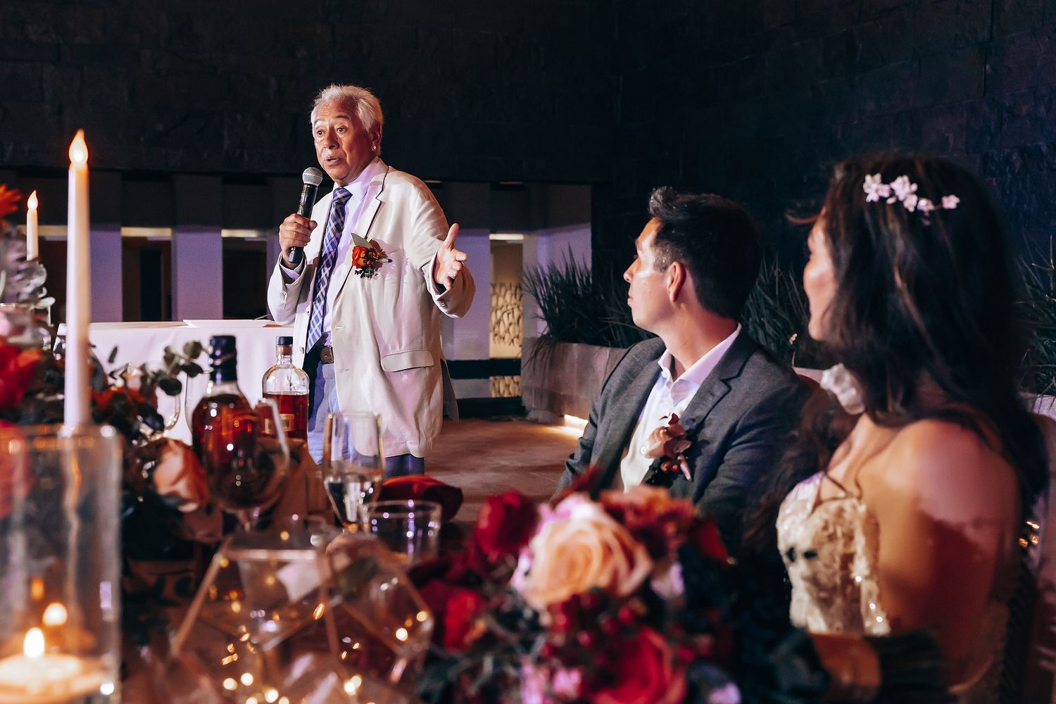 Wedding reception guests seated at tables with candlelight and floral centerpieces.