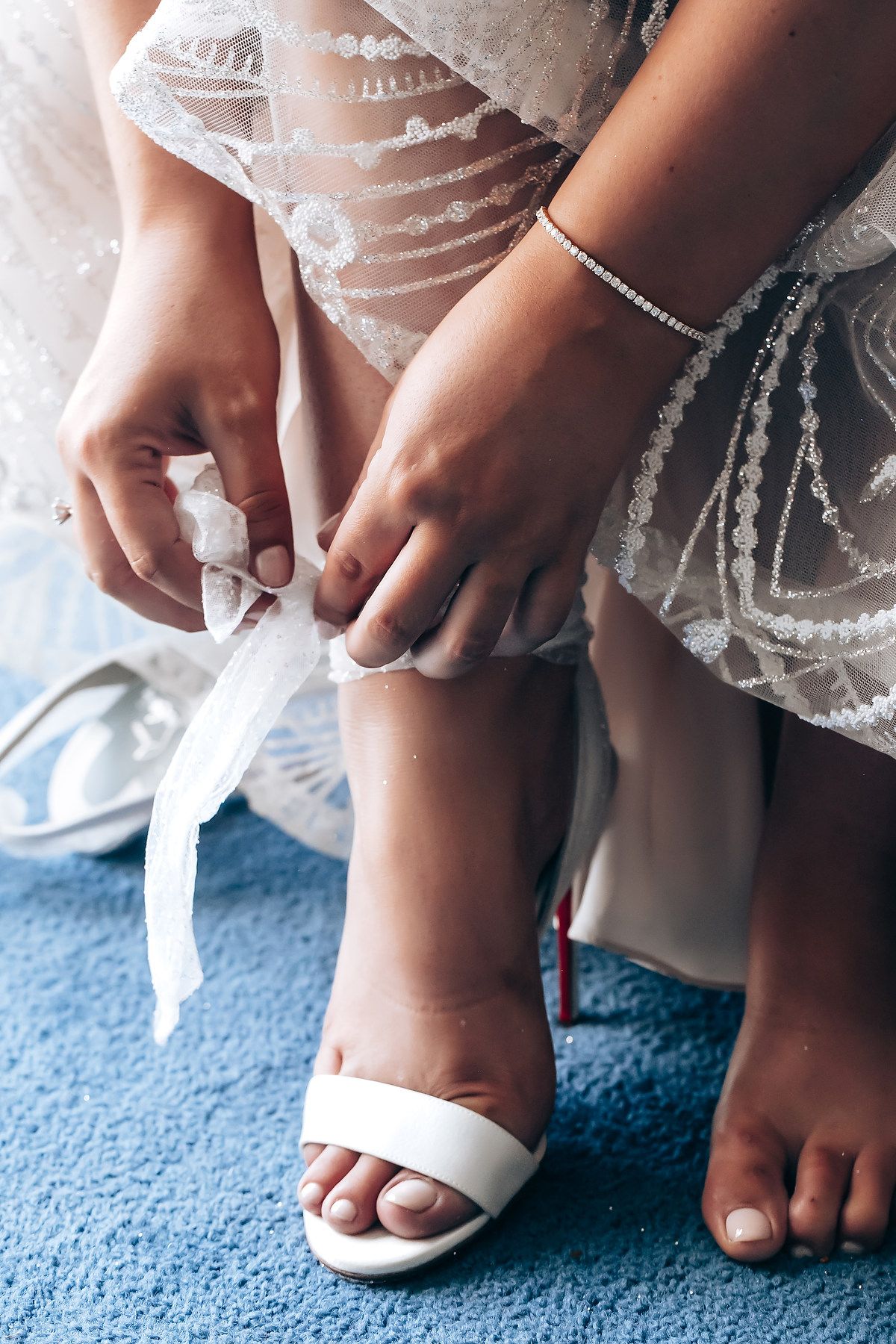 Close-up of white wedding shoes being put on feet against blue carpet.
