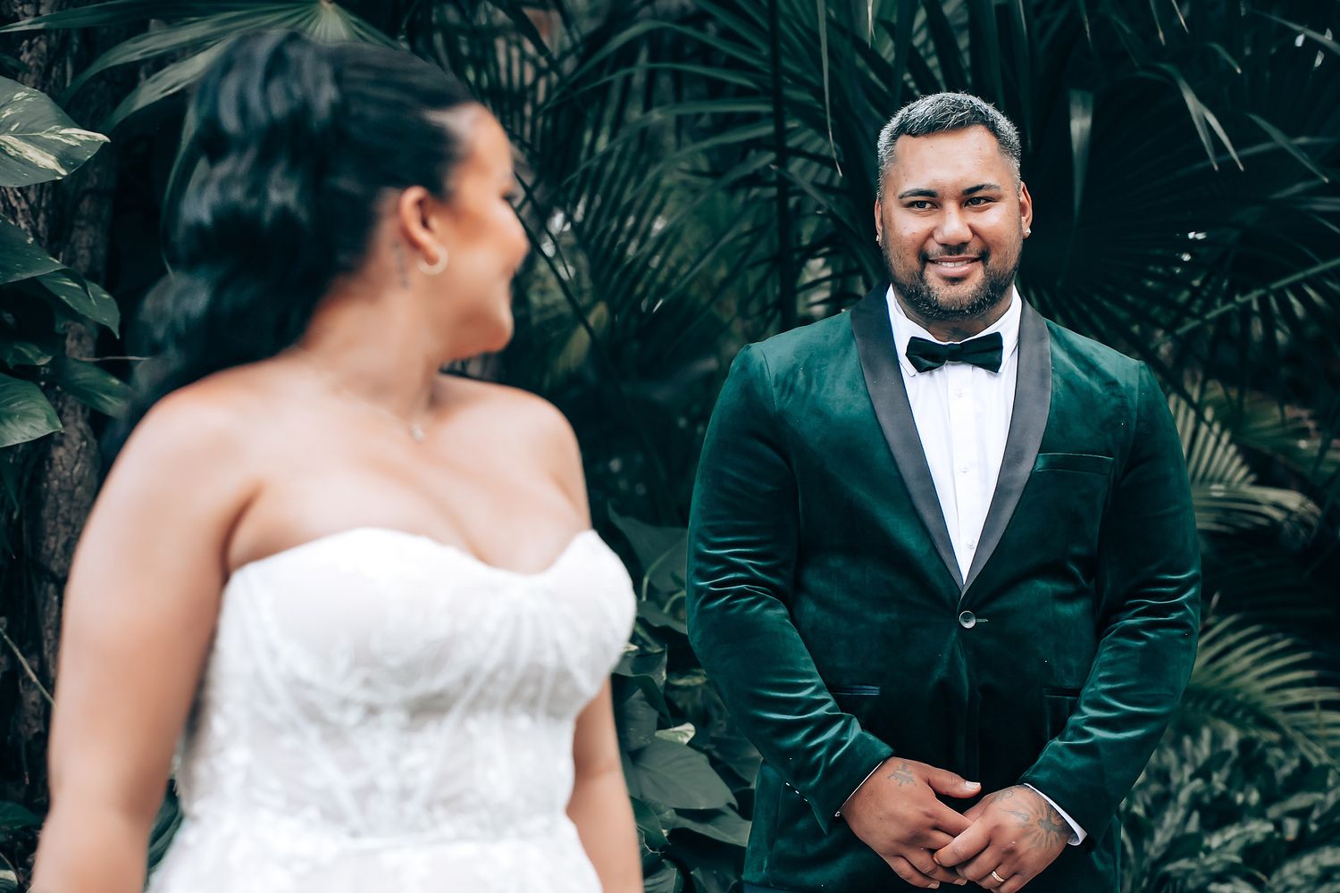 Wedding couple poses together in a lush tropical garden setting with natural lighting.