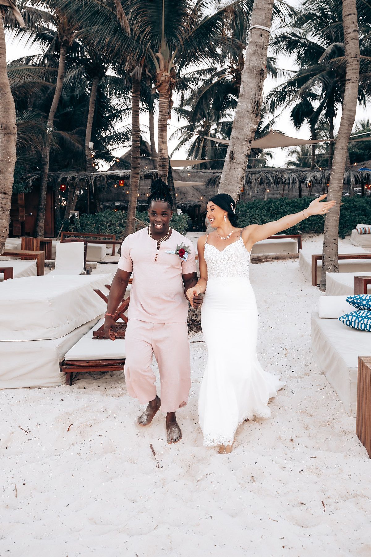 A group of people in white clothing dance and celebrate in a tropical setting.