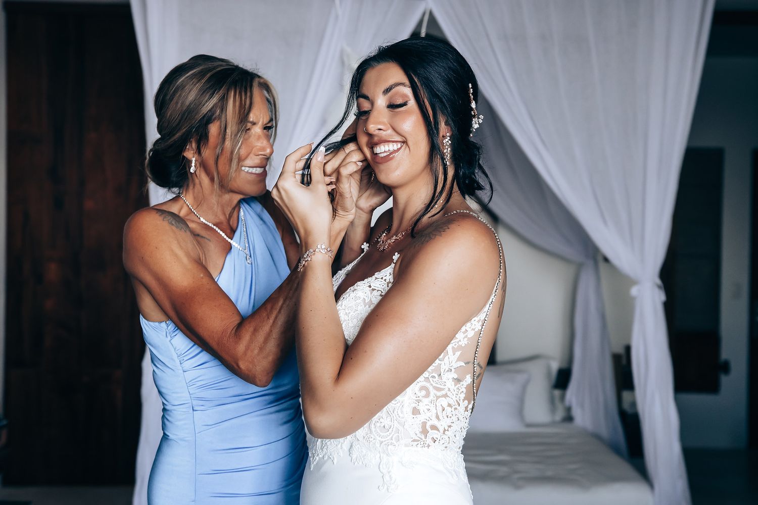 Two women in formal dresses embrace and smile at each other.