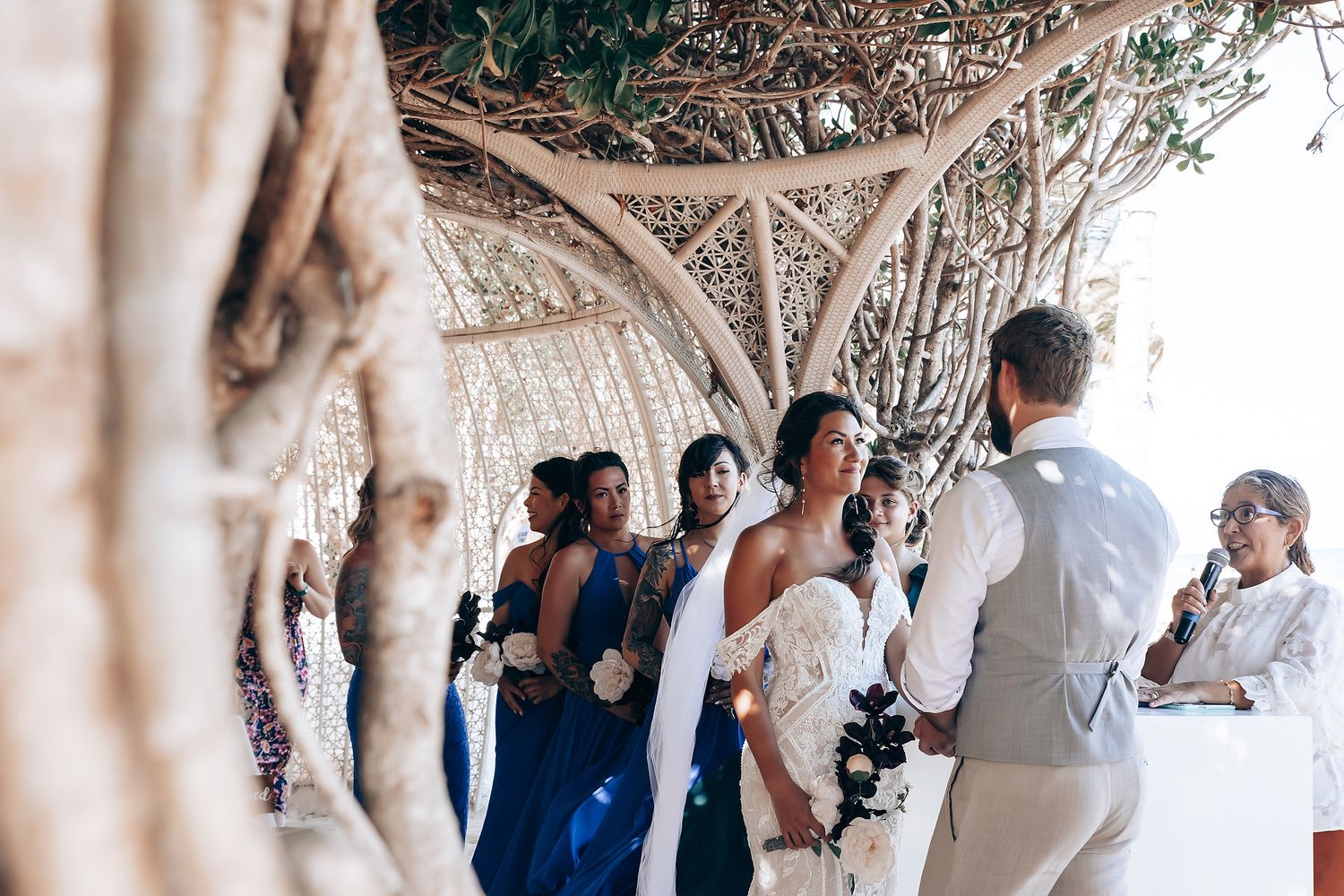 Wedding celebration under a white latticed canopy with tropical foliage.