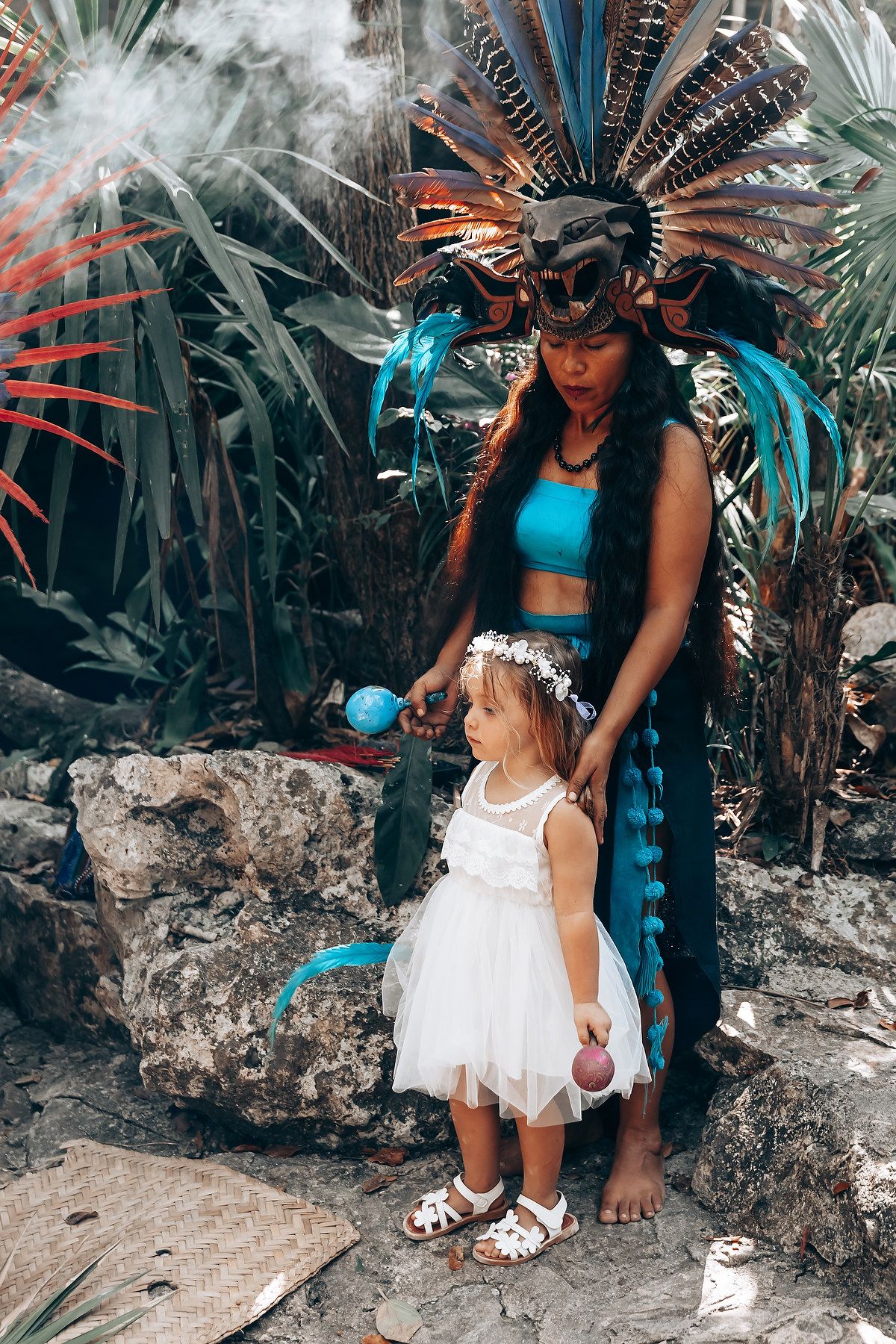 Traditional ceremonial attire featuring feathered headdress and white dress in tropical setting.