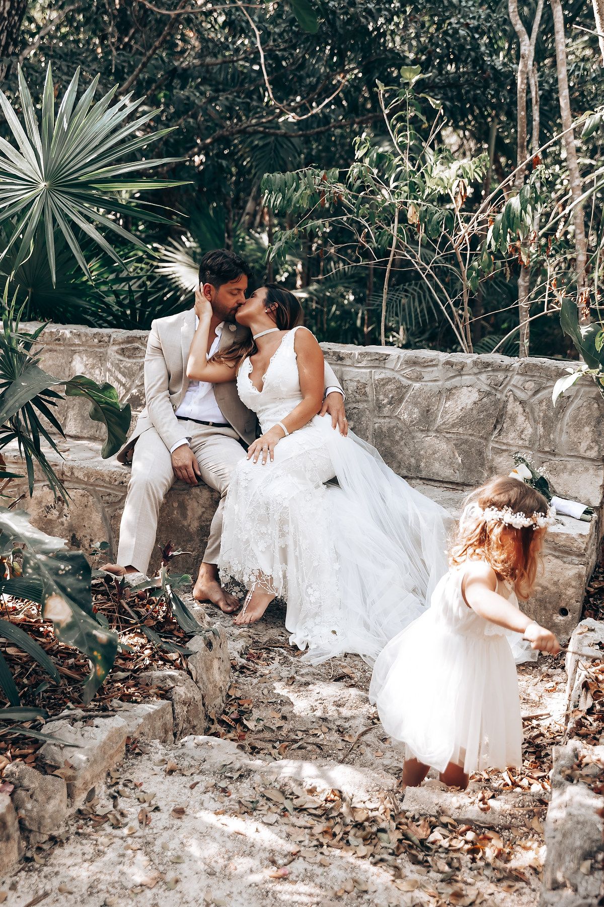 A romantic moment captured on stone steps surrounded by tropical plants and fallen leaves.