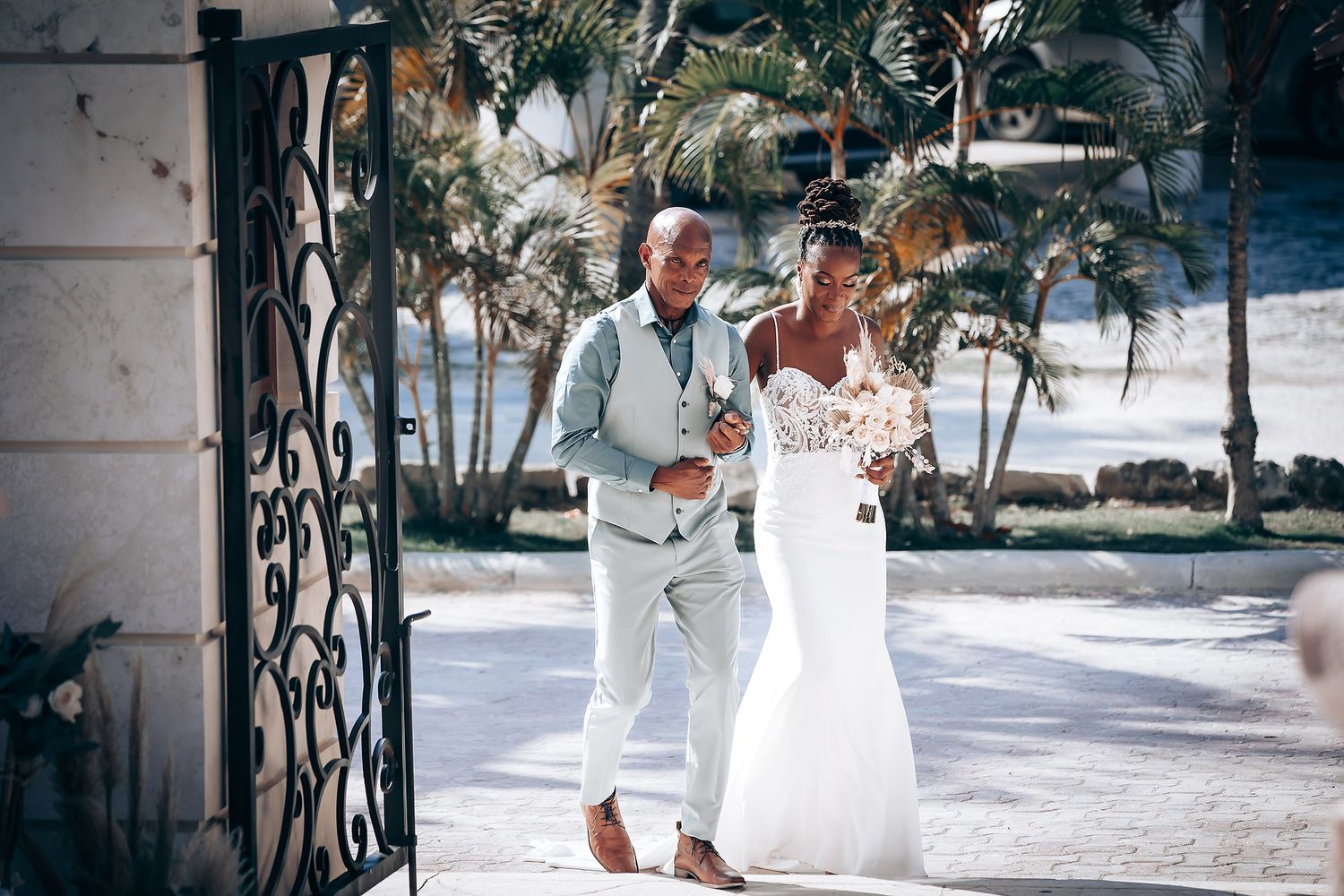 Wedding party walking along a palm-lined path in white attire.