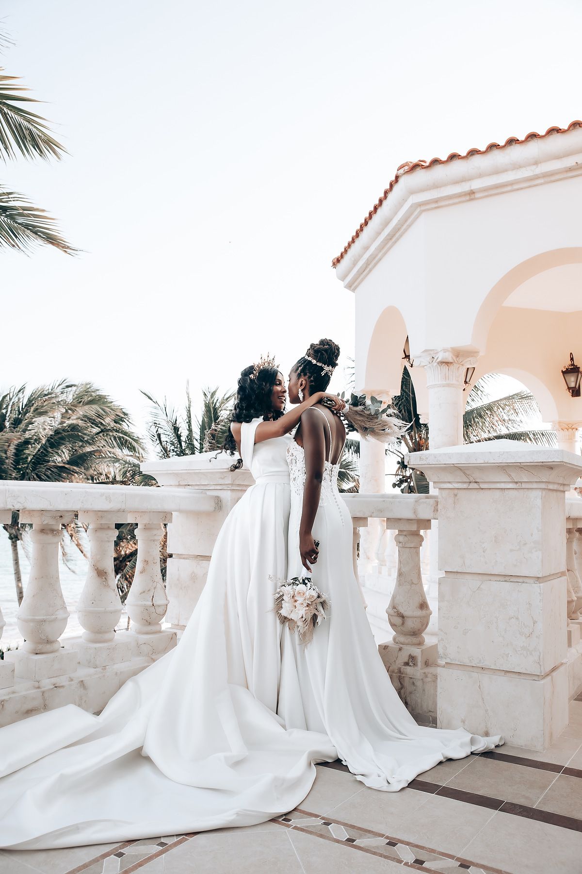 Row of white wedding dresses against Mediterranean-style balcony with stone balustrades and palm trees.
