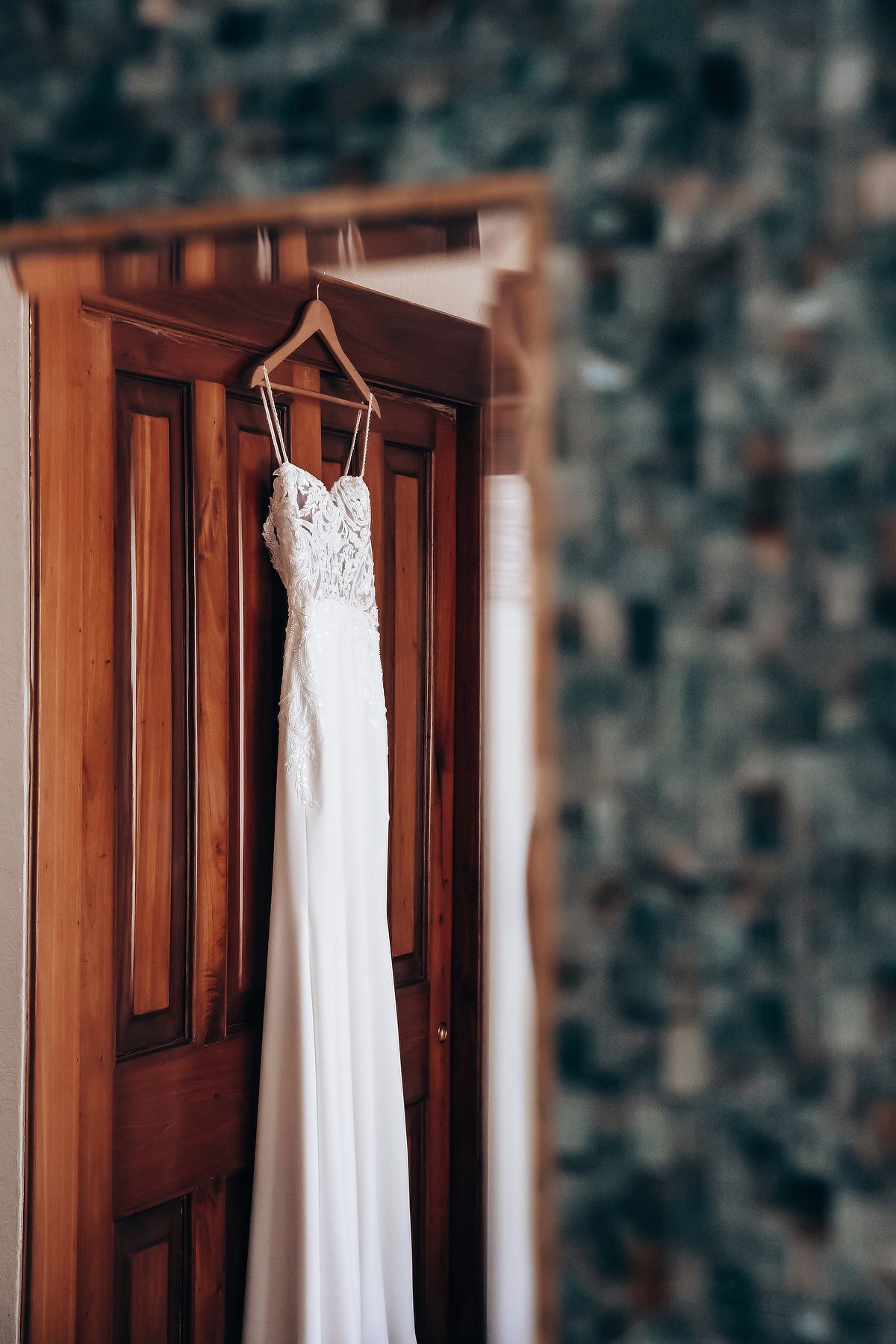 White wedding dress hanging on wooden door in elegant bridal preparation room.