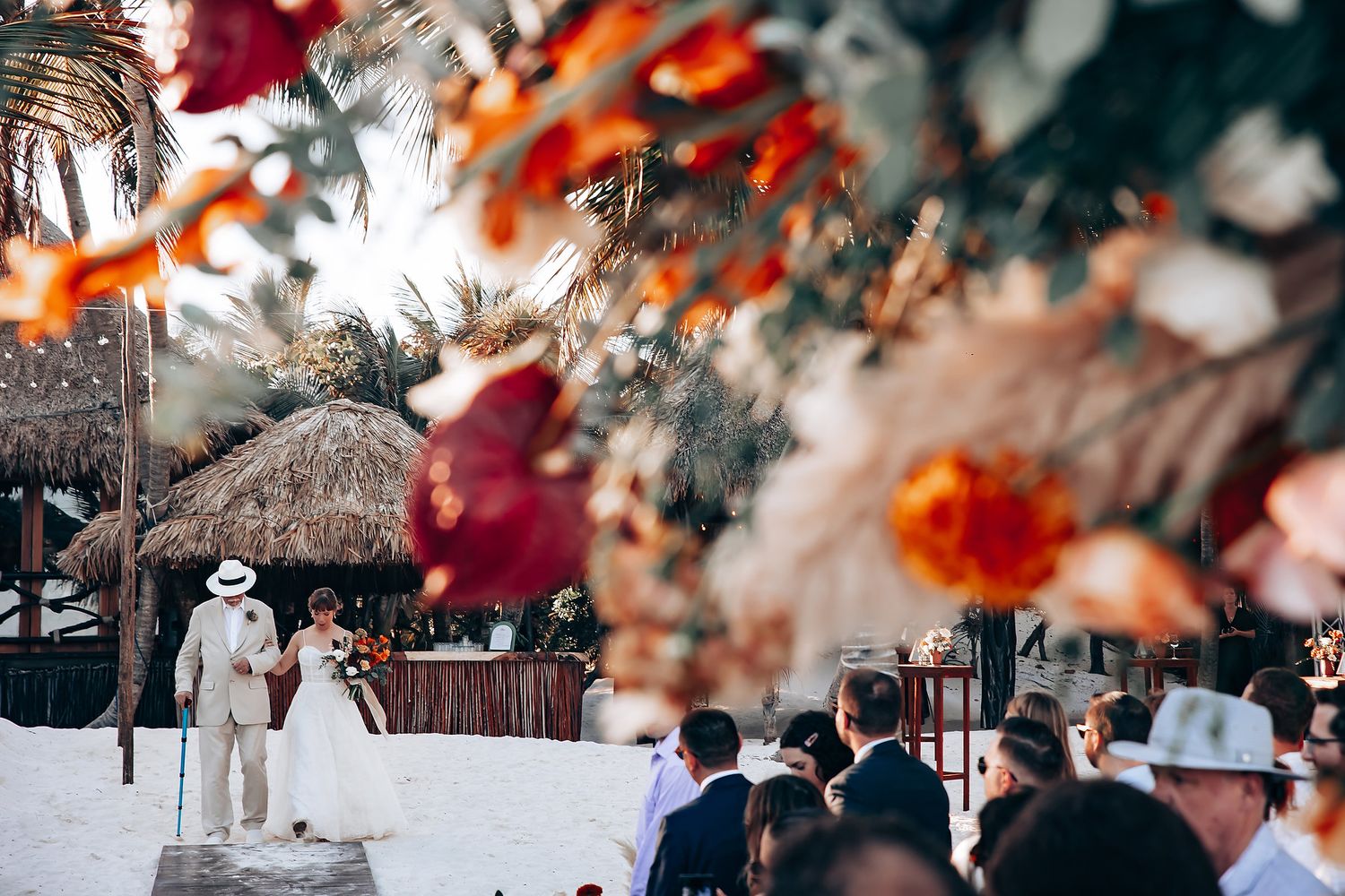 Elegant beach wedding reception with vibrant red and orange floral arrangements under palm trees.