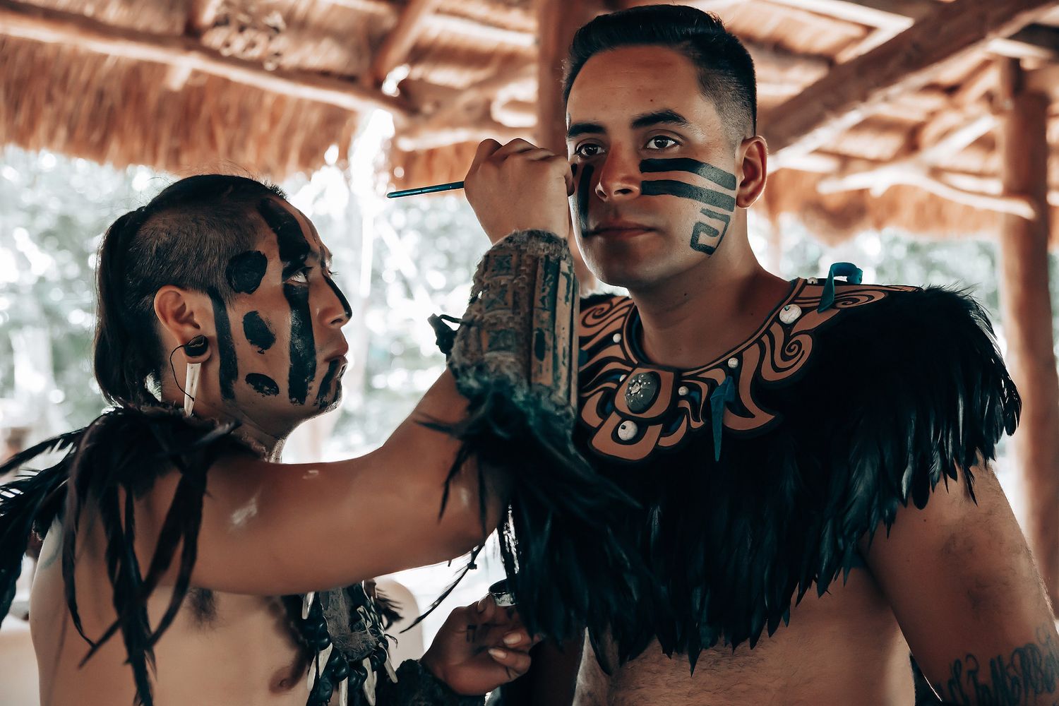 Two men in traditional Mayan costumes with face paint and feathers during a cultural ritual.