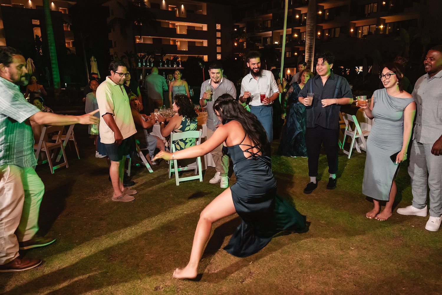Woman dancing energetically at an outdoor evening party while guests watch and socialize on a grass venue.