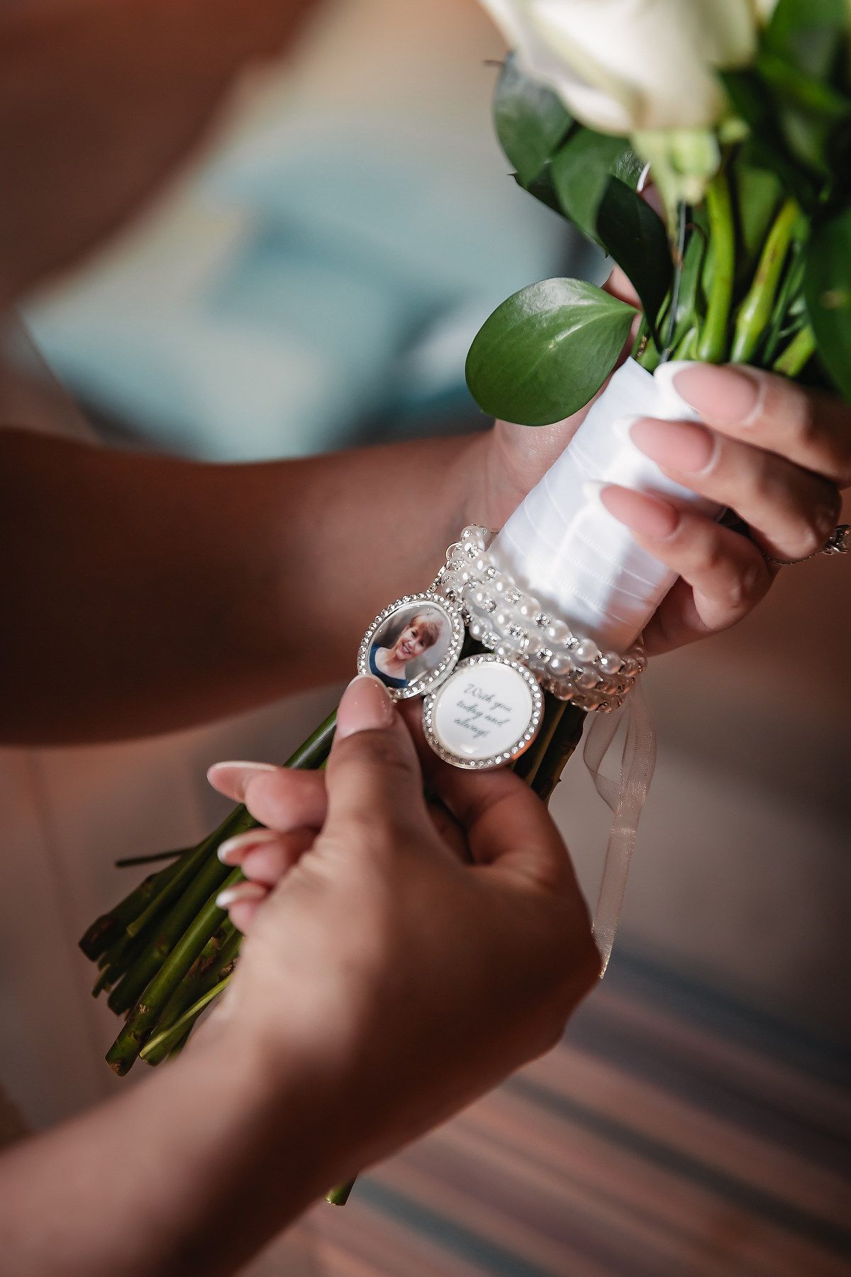 Close-up of bridal bouquet with pearl bracelet charm featuring a memorial photo locket on white roses.