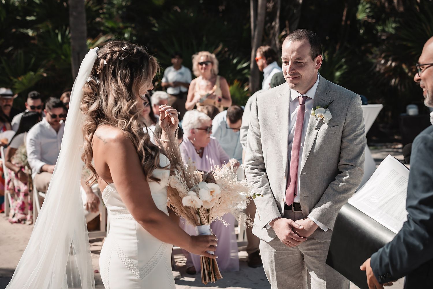 Bride and groom exchange vows at an outdoor wedding ceremony surrounded by seated guests.