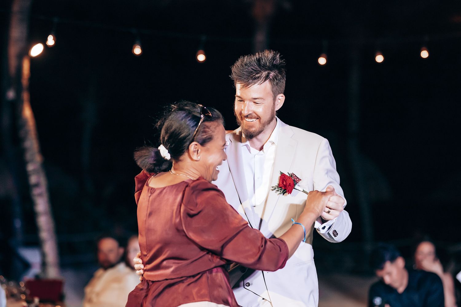 Evening outdoor wedding dance with string lights and trees creating magical atmosphere.