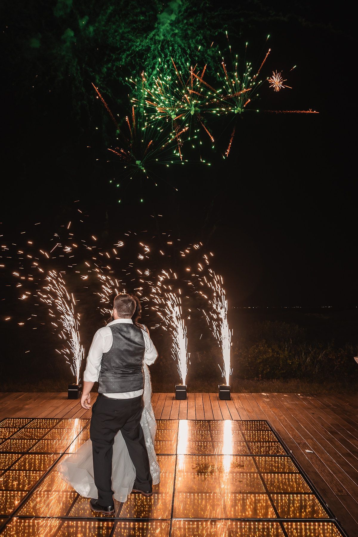Colorful fireworks and sparklers illuminate a wooden deck during a nighttime celebration.