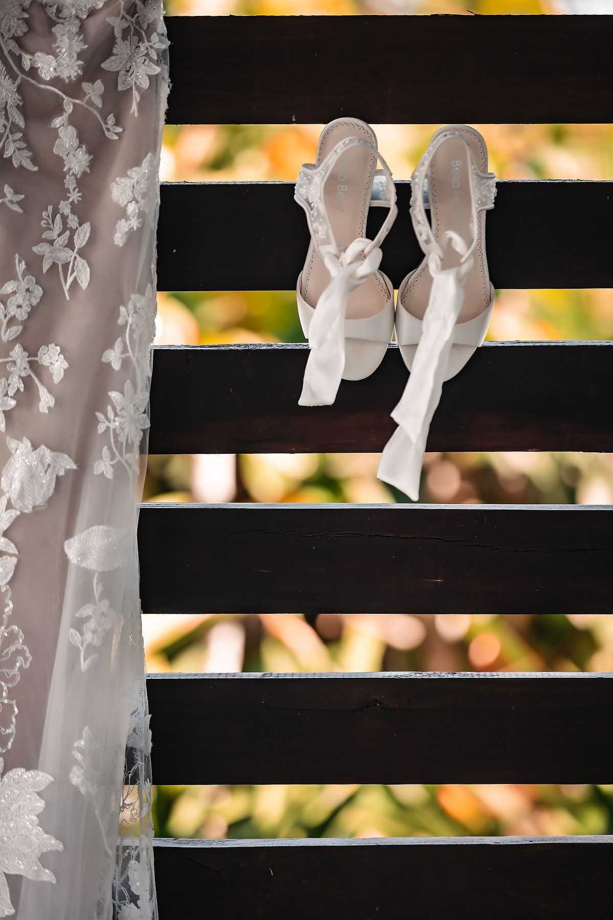 White bridal ballet shoes displayed on black and white striped wooden slats.