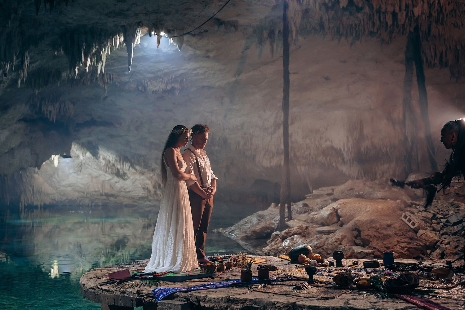 A spiritual ceremony unfolds in a dramatic cave setting with natural rock formations and dim lighting.