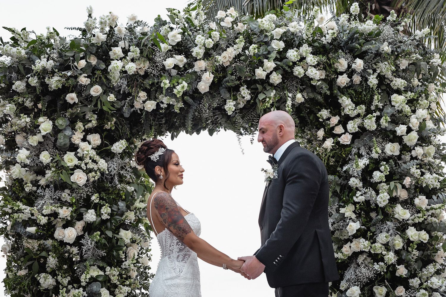 A wedding ceremony setup with an elegant white floral arch and chairs arranged outdoors.